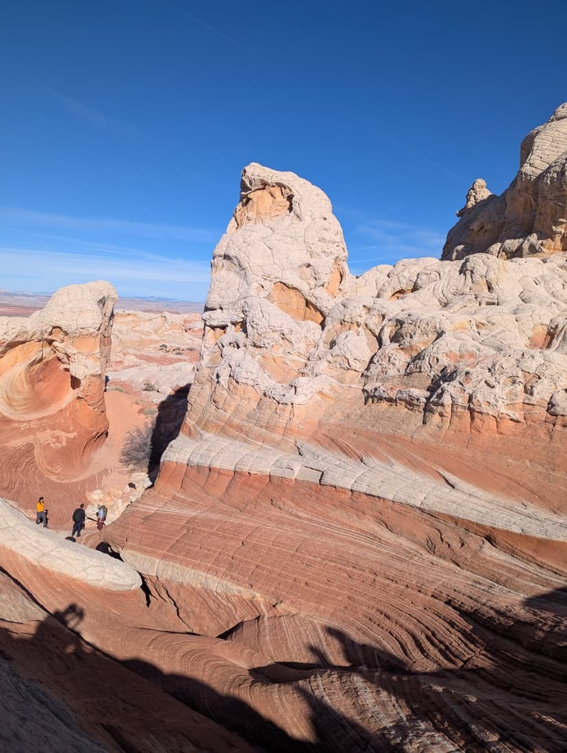 White Pocket rock formations with layered red sandstone and hikers exploring