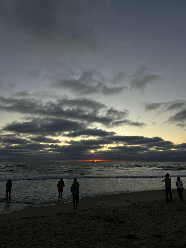Sunset at a California beach with silhouettes of people watching the horizon