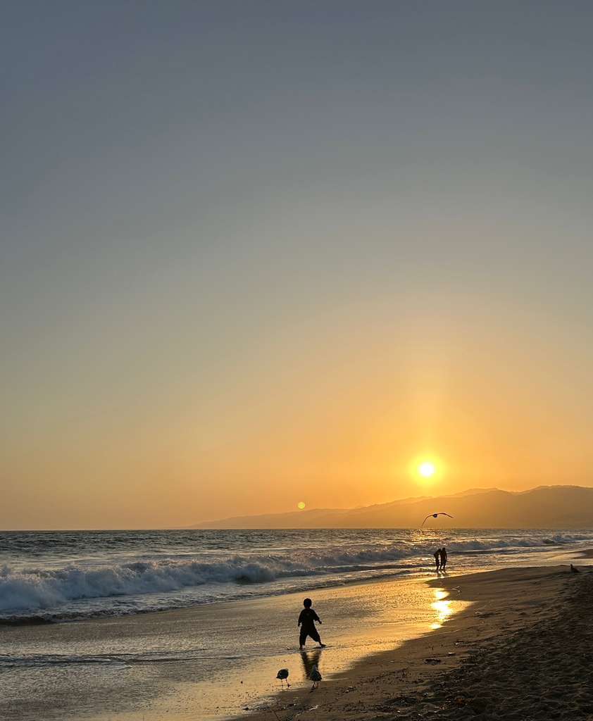 Golden hour at the beach with waves and people walking along the shore