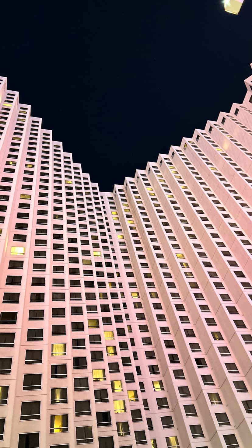 Tall modern hotel building lit in soft pink under the night sky