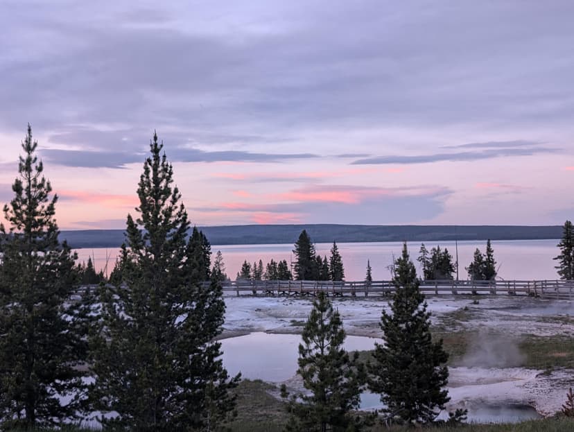 Pastel evening sky over Yellowstone Lake with pine trees and thermal pools in the foreground