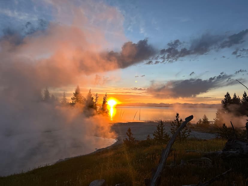 Steam rising from Yellowstone geysers during sunrise with the sun reflecting over the lake
