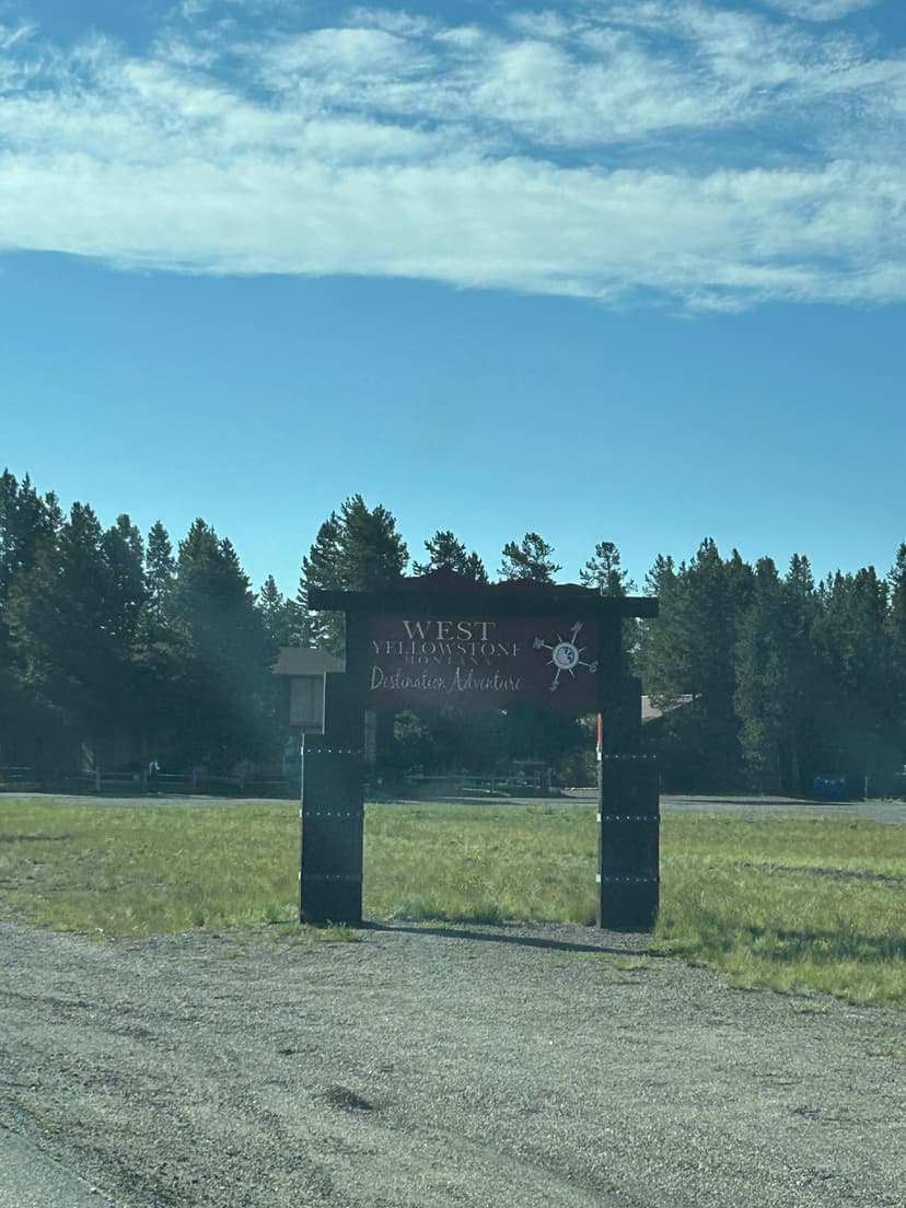 West Yellowstone entrance sign under a bright blue sky surrounded by pine trees