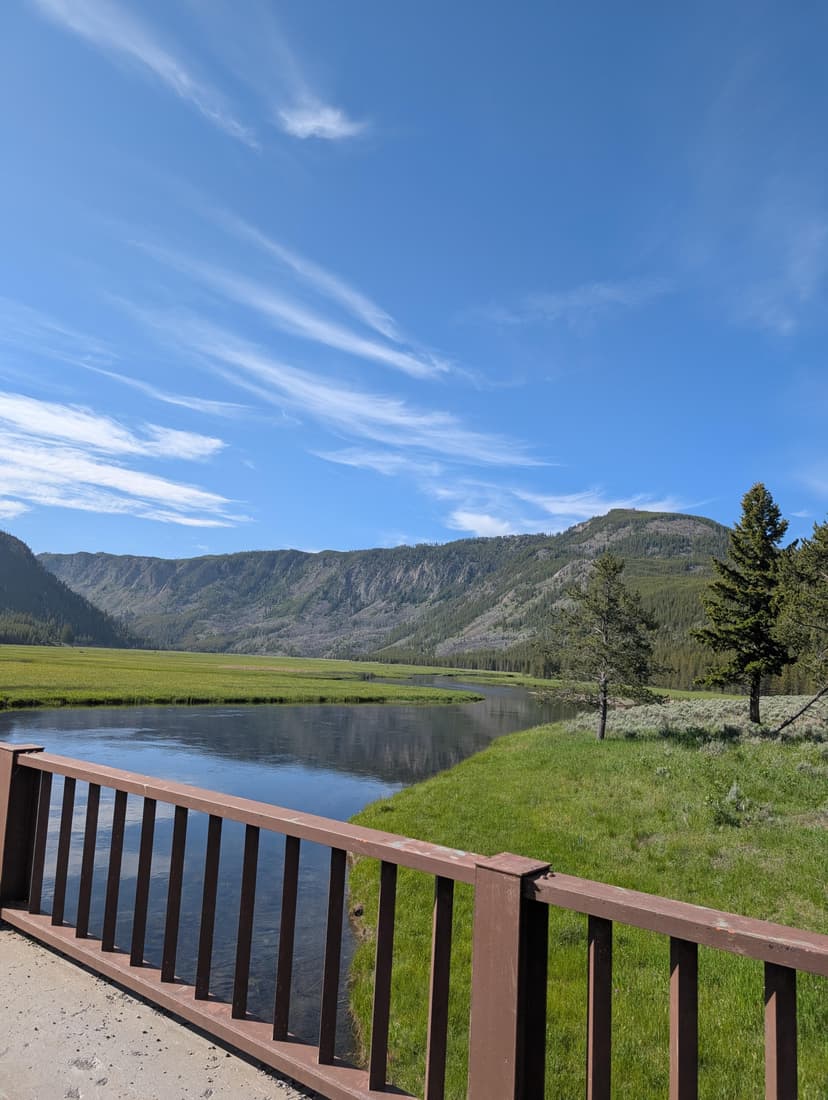 Bridge view over a calm river running through a green valley with mountains in the distance