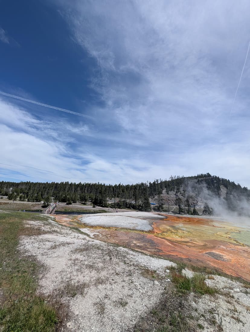 Colorful geothermal area with mineral deposits and steam vents under a clear sky