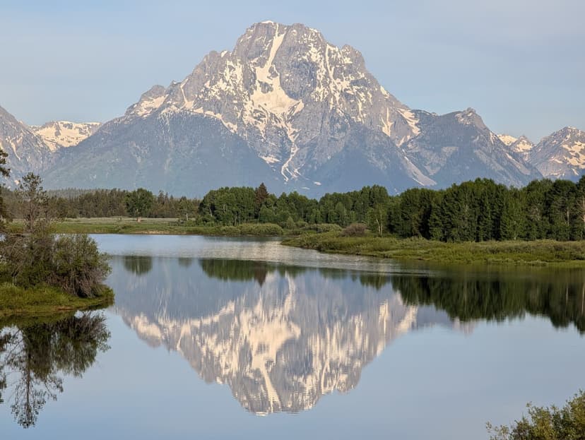 Snow-covered Grand Teton mountain reflected in still lake waters on a clear morning